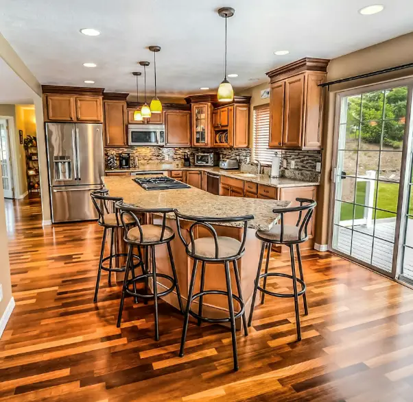 An elegant kitchen with wood floors, and island with chairs, and stainless steel appliances.