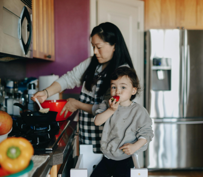 A mother cooking with her child. The little boy is taking a bite.