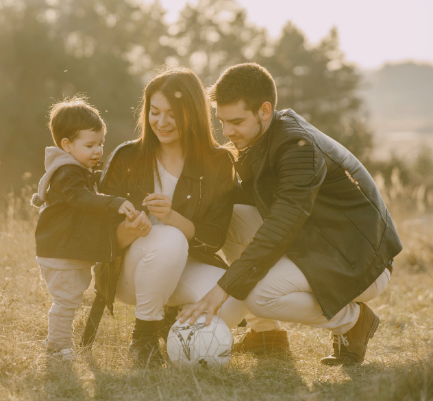 A happy couple in the park with their son. Dad is holding a soccer ball.