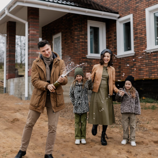 Man popping Champagne bottle with this family in the background at new home build site.