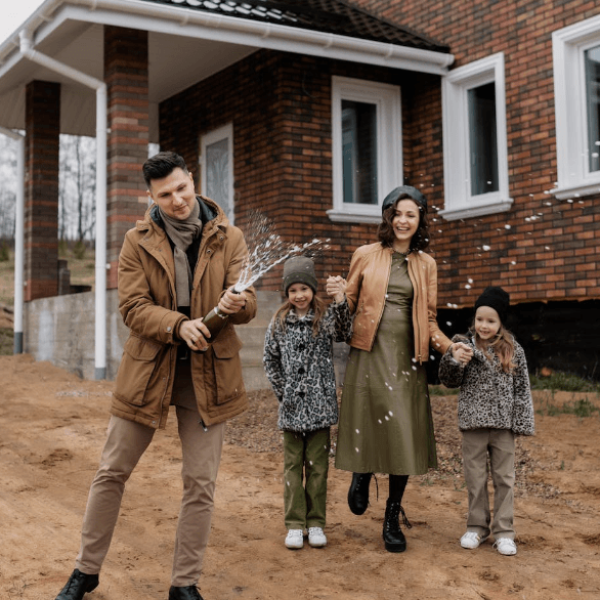Man popping Champagne bottle with this family in the background at new home build site.