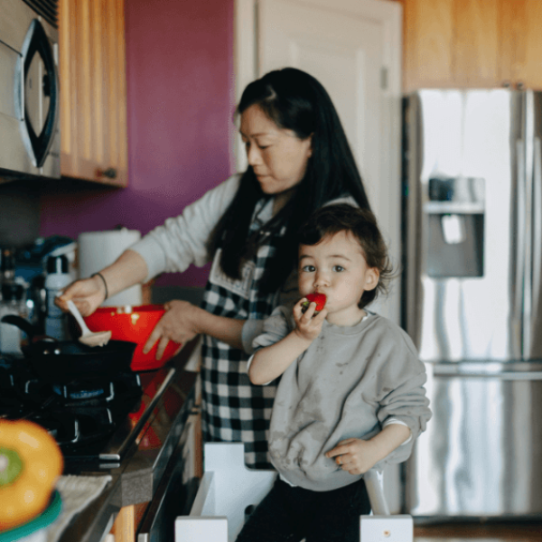 A mother cooking with her child. The little boy is taking a bite.