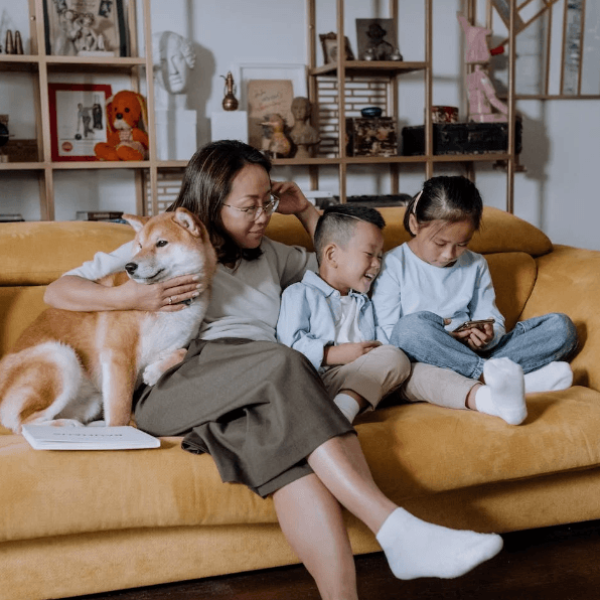 A mother sitting with her two kids and her dog on their couch while the little girl is playing on her phone.