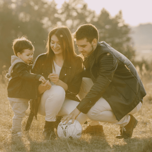 A happy couple in the park with their son. Dad is holding a soccer ball.
